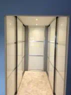 U shapped sliding wardrobe in pearl white glass split into thirds with polished silver frames